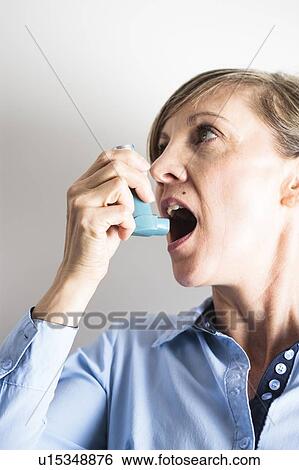 Stock Photograph - Woman using an inhaler to treat an asthma attack. The inhaler contains bronchodilator drugs, which widen constricted airways in the lungs.. Fotosearch