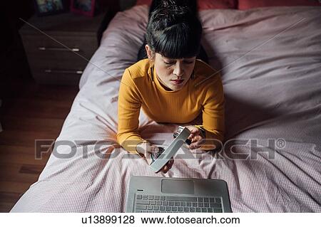 Woman using headphones with laptop on bed View Large Photo Image Stock Photo - Woman using headphones with laptop on bed. Fotosearch