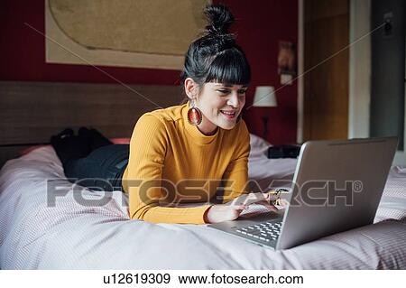 Stock Photo - Woman using laptop on bed. Fotosearch