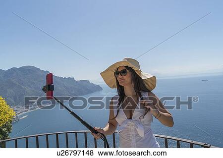 Stock Photo - Woman using selfie stick by sea. Fotosearch