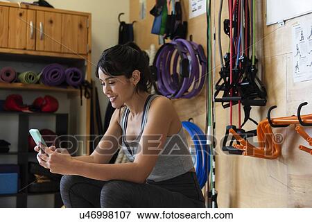 Stock Photo - Woman using smart phone in gym. Fotosearch