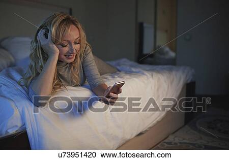 Woman using smart phone while lying on bed View Large Photo Image Stock Image - Woman using smart phone while lying on bed. Fotosearch