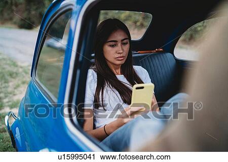 Stock Image - Woman using smartphone inside car. Fotosearch