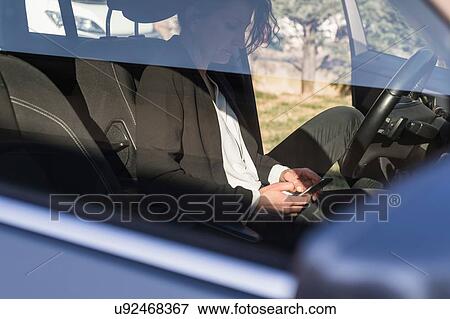 Stock Photo - Woman using smartphone inside vehicle. Fotosearch