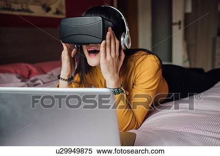 Stock Photography - Woman using VR headset on bed. Fotosearch