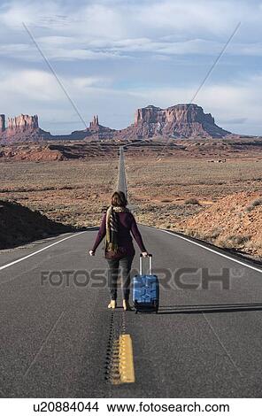 Picture - Woman walking with suitcase on road through Monument Valley, Utah, USA. Fotosearch