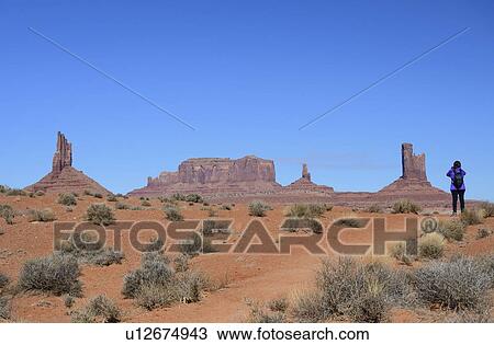 Stock Image - Woman wearing backpack by buttes in Monument Valley, Arizona, USA. Fotosearch
