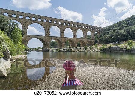 Stock Image - Woman wearing pink hat sunbathing by Pont du Gard in Vers-Pont-du-Gard, France. Fotosearch