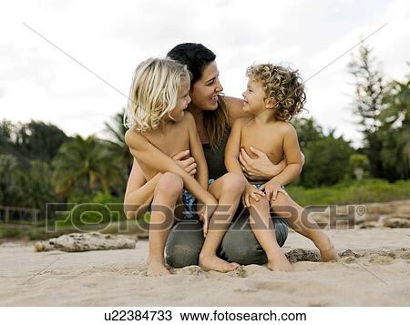 Woman with her sons sitting on her lap on beach View Large Photo Image Stock Image - Woman with her sons sitting on her lap on beach. Fotosearch