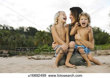 Stock Photo - Woman with her sons sitting on her lap on beach. Fotosearch