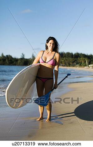 Stock Photo - Woman with paddleboard and oar on beach. Fotosearch