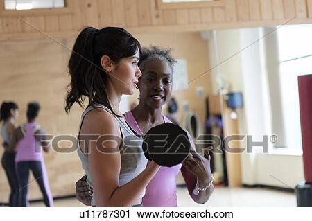 Stock Image - Woman with personal trainer lifting weights in gym. Fotosearch