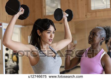 Stock Photography - Woman with personal trainer lifting weights in gym. Fotosearch