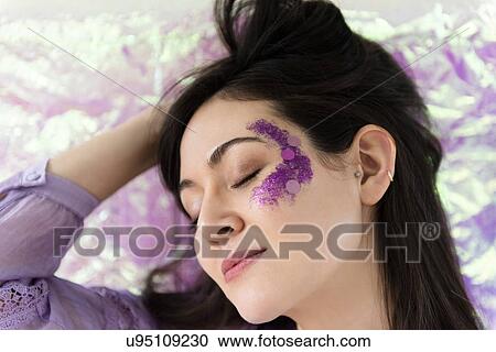 Stock Image - Woman with purple glitter on cheek. Fotosearch