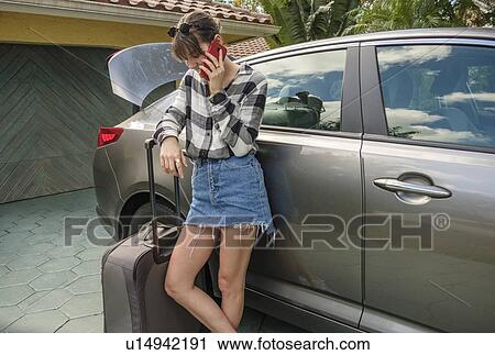 Stock Image - Woman with smart phone and suitcase by car. Fotosearch