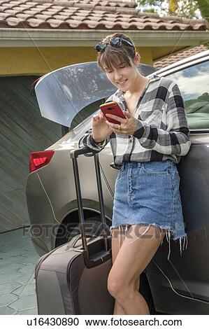 Stock Image - Woman with smart phone and suitcase by car. Fotosearch