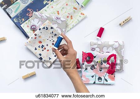 Stock Photo - Woman's hand holding blue thread above variety of fabrics. Fotosearch