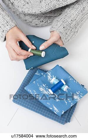 Picture - Woman's hand matching thread to blue fabric. Fotosearch