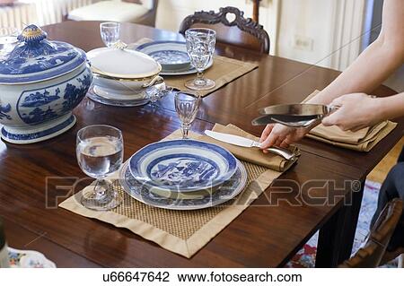 Stock Image - Woman's hands setting table with antique tableware. Fotosearch