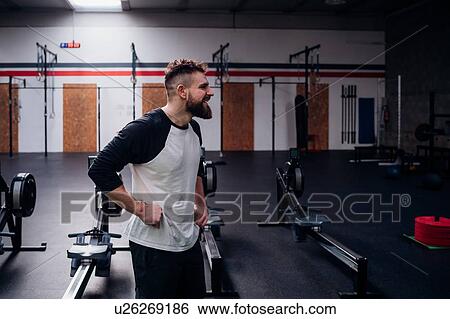 Stock Photograph - Young bearded man training, standing with hands on hips in gym. Fotosearch