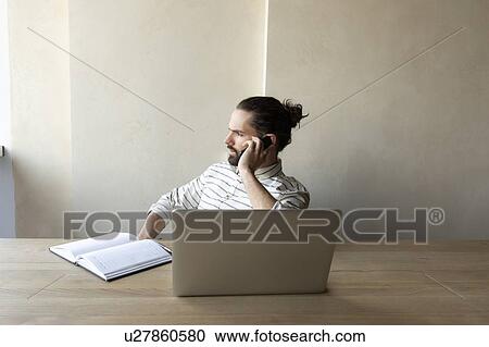 Stock Image - Young businessman on phone by laptop. Fotosearch