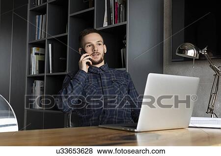 Stock Photo - Young businessman on phone by laptop. Fotosearch