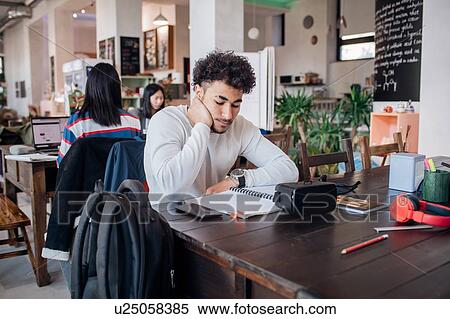 Stock Photography - Young businessman remote working on laptop at cafe table. Fotosearch