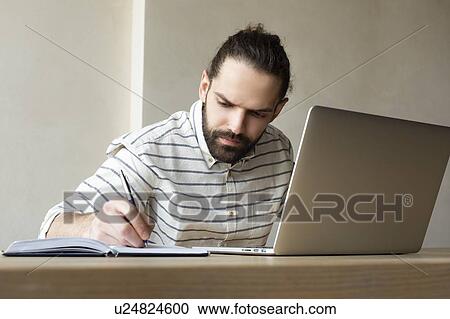 Young businessman with laptop writing in note pad View Large Photo Image Stock Image - Young businessman with laptop writing in note pad. Fotosearch