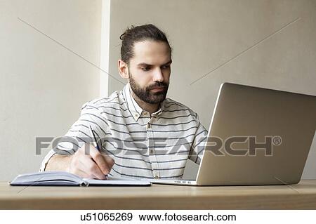 Young businessman with laptop writing in note pad View Large Photo Image Stock Photo - Young businessman with laptop writing in note pad. Fotosearch