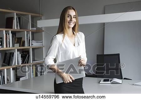 Stock Photograph - Young businesswoman holding laptop in office. Fotosearch