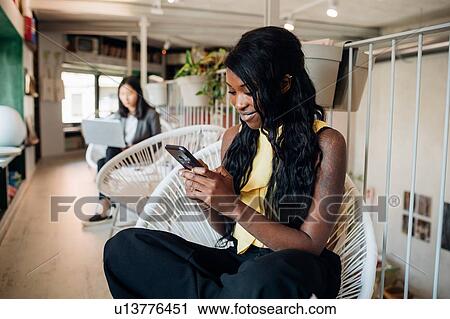 Stock Image - Young businesswoman looking at smartphone in cafe. Fotosearch