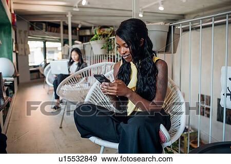 Stock Photo - Young businesswoman looking at smartphone in cafe. Fotosearch