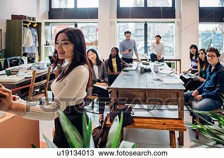 Stock Image - Young businesswoman making presentation for colleagues. Fotosearch