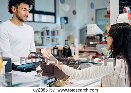 Young businesswoman making smartphone payment at cafe counter View Large Photo Image Stock Photo - Young businesswoman making smartphone payment at cafe counter. Fotosearch