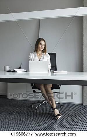 Young businesswoman sitting at desk View Large Photo Image Stock Photo - Young businesswoman sitting at desk. Fotosearch