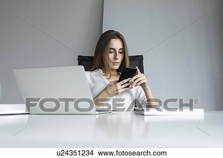 Picture - Young businesswoman text messaging at desk. Fotosearch