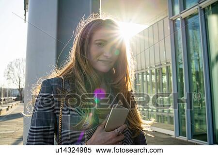 Stock Photography - Young businesswoman with smartphone outside office building, portrait, Turin, Piemonte, Italy. Fotosearch
