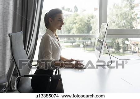 Picture - Young businesswoman working on desktop computer. Fotosearch