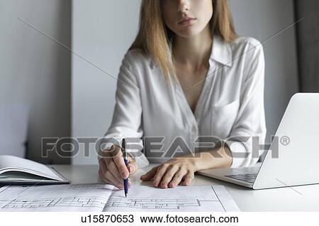 Stock Image - Young businesswoman working on blueprints. Fotosearch