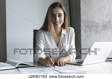 Stock Image - Young businesswoman working on blueprints. Fotosearch