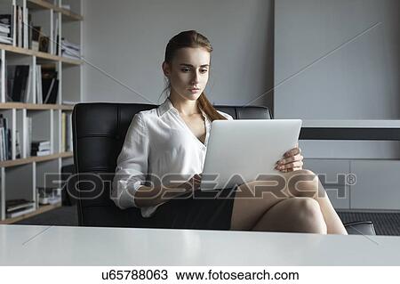Stock Image - Young businesswoman working with laptop on sofa. Fotosearch