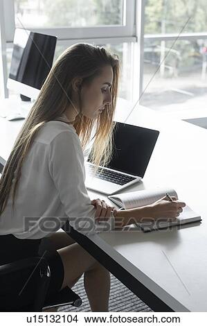 Picture - Young businesswoman writing notes at desk. Fotosearch