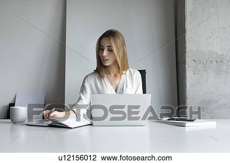 Young businesswoman writing notes while working on laptop View Large Photo Image Stock Image - Young businesswoman writing notes while working on laptop. Fotosearch