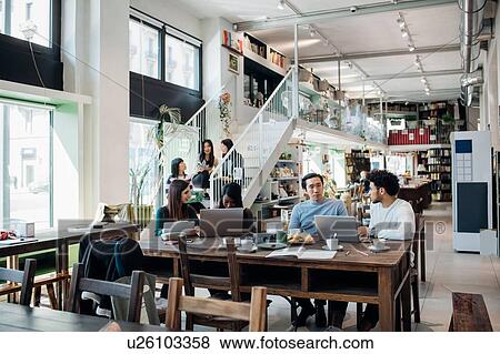 Young businesswomen and businessmen remote working having meeting at cafe table View Large Photo Image Stock Photo - Young businesswomen and businessmen remote working having meeting at cafe table. Fotosearch