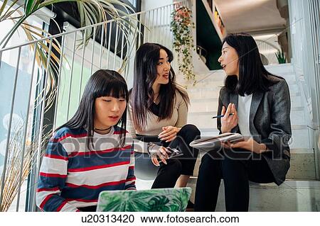 Stock Image - Young businesswomen having team meeting on stairway. Fotosearch