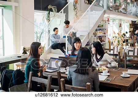 Stock Image - Young businesswomen remote working having meeting at cafe table. Fotosearch