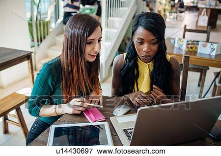 Stock Photo - Young businesswomen remote working, looking at laptop in cafe. Fotosearch
