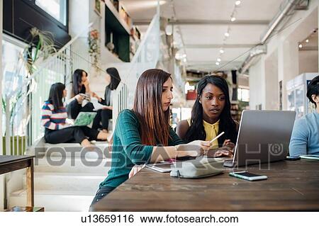 Stock Photograph - Young businesswomen remote working, looking at laptop in cafe. Fotosearch