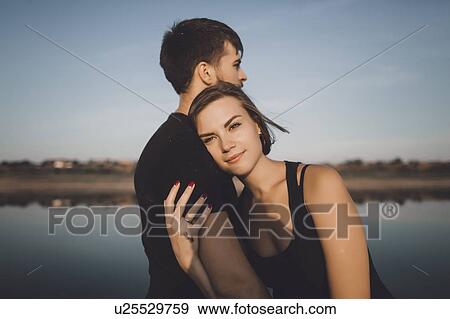 Young couple embracing by lake View Large Photo Image Stock Photo - Young couple embracing by lake. Fotosearch