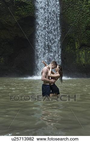 Stock Image - Young couple embracing in river by Tibumana Waterfall in Bali, Indonesia. Fotosearch